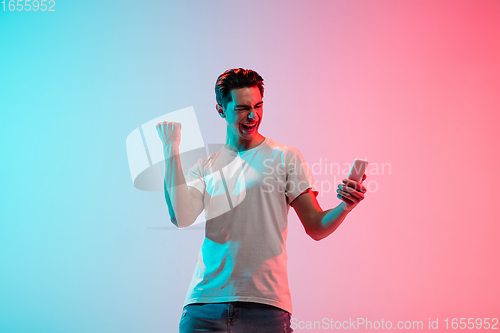 Image of Young caucasian man\'s portrait on gradient blue-pink studio background in neon light