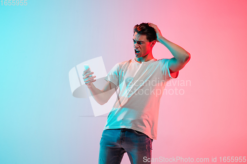 Image of Young caucasian man\'s portrait on gradient blue-pink studio background in neon light