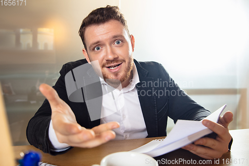 Image of Young man talking, working during videoconference with colleagues at home office