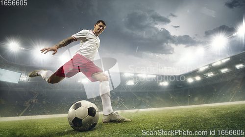 Image of Young man football player kicking ball while match at stadium. Flyer for ad, design.