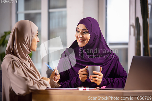 Image of Happy two muslim women at home during lesson, studying near computer, online education