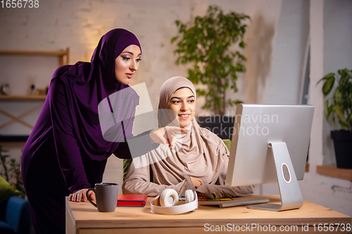 Image of Happy two muslim women at home during lesson, studying near computer, online education