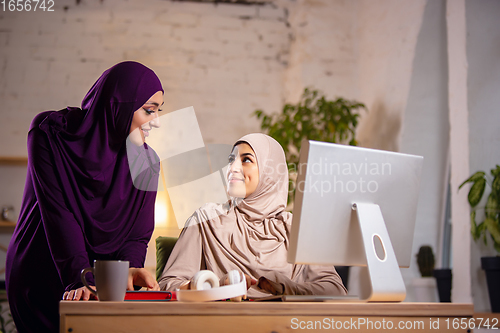 Image of Happy two muslim women at home during lesson, studying near computer, online education