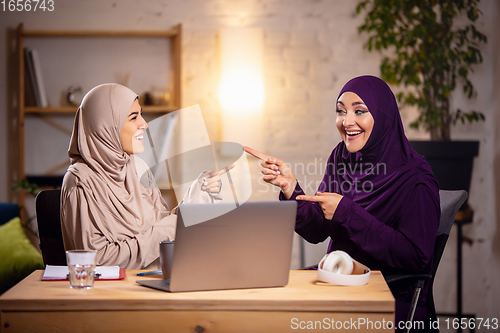 Image of Happy two muslim women at home during lesson, studying near computer, online education