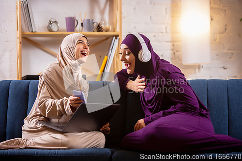 Image of Happy two muslim women at home talking, smiling, having fun. Friendship, modern tech, emotions concept