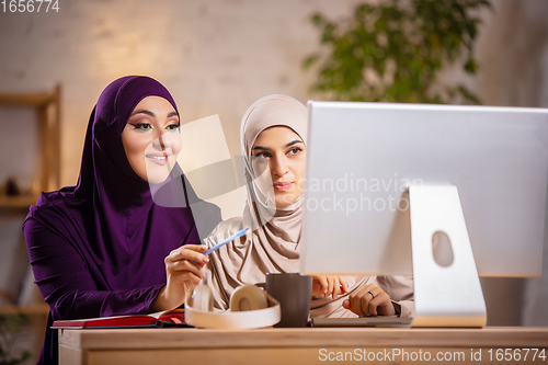 Image of Happy two muslim women at home during lesson, studying near computer, online education