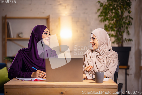 Image of Happy two muslim women at home during lesson, studying near computer, online education