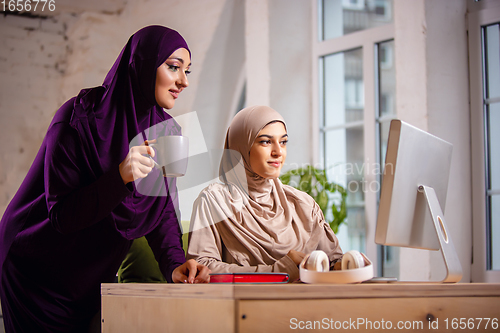 Image of Happy two muslim women at home during lesson, studying near computer, online education