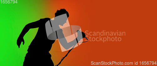 Image of Silhouette of young caucasian male singer isolated on green-orange gradient studio background in neon light