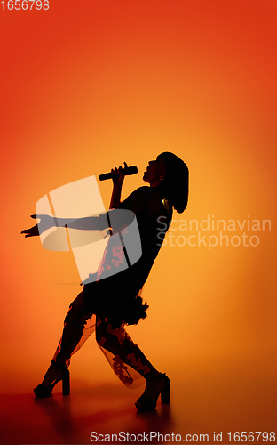 Image of Silhouette of young caucasian female singer isolated on orange gradient studio background in neon light