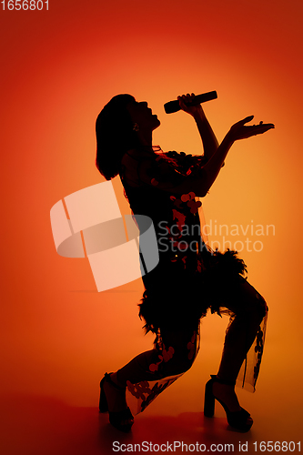 Image of Silhouette of young caucasian female singer isolated on orange gradient studio background in neon light