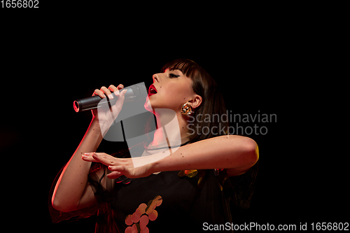 Image of Caucasian female singer portrait isolated on dark studio background in neon light