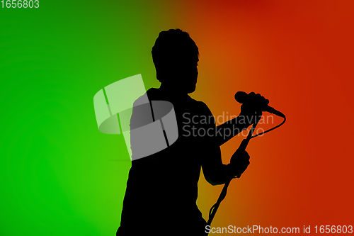 Image of Silhouette of young caucasian male singer isolated on green-orange gradient studio background in neon light