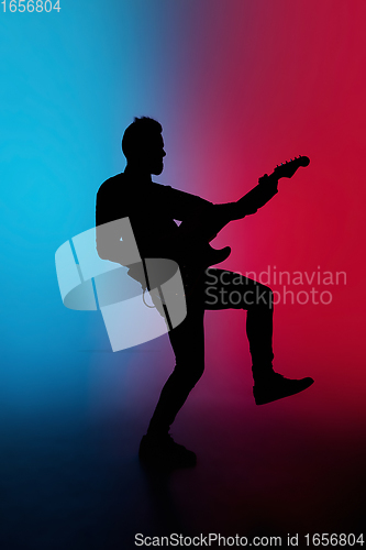 Image of Silhouette of young caucasian male guitarist isolated on blue-pink gradient studio background in neon light