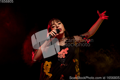 Image of Caucasian female singer portrait isolated on dark studio background in neon light