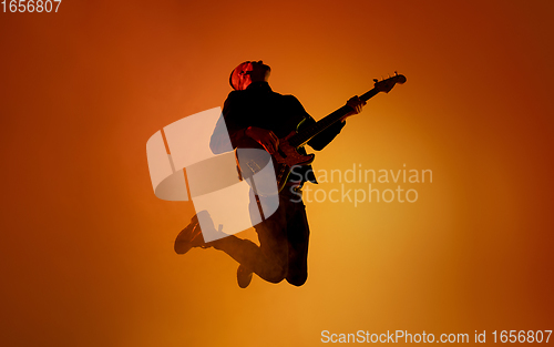 Image of Silhouette of young caucasian male guitarist isolated on orange gradient studio background in neon light