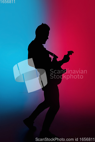 Image of Silhouette of young caucasian male guitarist isolated on blue-pink gradient studio background in neon light