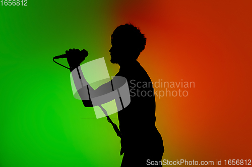 Image of Silhouette of young caucasian male singer isolated on green-orange gradient studio background in neon light