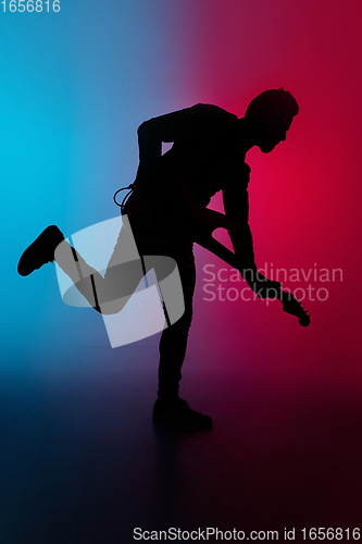 Image of Silhouette of young caucasian male guitarist isolated on blue-pink gradient studio background in neon light