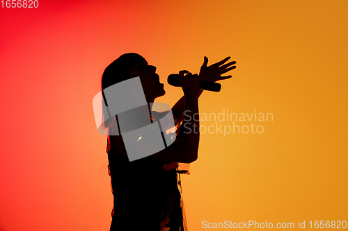 Image of Silhouette of young caucasian female singer isolated on orange gradient studio background in neon light