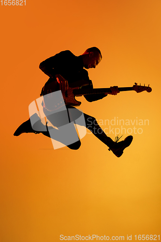 Image of Silhouette of young caucasian male guitarist isolated on orange gradient studio background in neon light