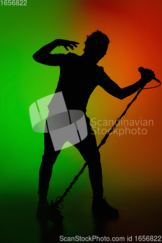 Image of Silhouette of young caucasian male singer isolated on green-orange gradient studio background in neon light