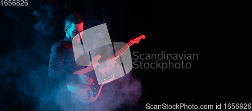 Image of Silhouette of young caucasian male guitarist isolated on blue-pink gradient studio background in neon light