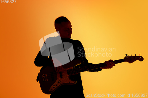 Image of Silhouette of young caucasian male guitarist isolated on orange gradient studio background in neon light
