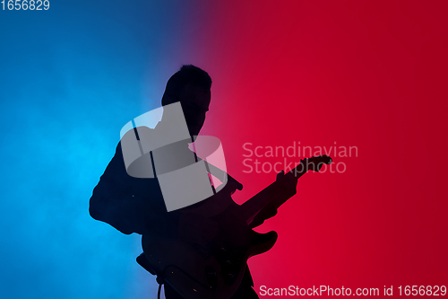 Image of Silhouette of young caucasian male guitarist isolated on blue-pink gradient studio background in neon light