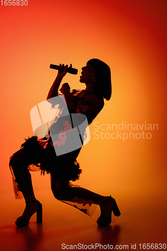 Image of Silhouette of young caucasian female singer isolated on orange gradient studio background in neon light