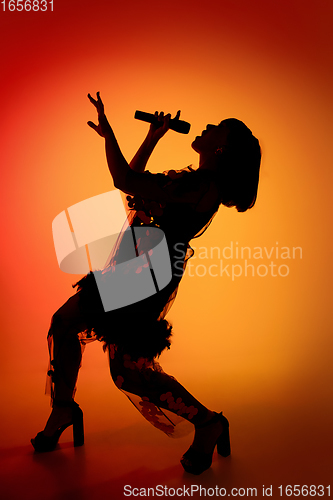 Image of Silhouette of young caucasian female singer isolated on orange gradient studio background in neon light