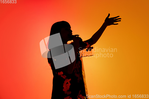 Image of Silhouette of young caucasian female singer isolated on orange gradient studio background in neon light