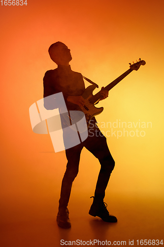 Image of Silhouette of young caucasian male guitarist isolated on orange gradient studio background in neon light