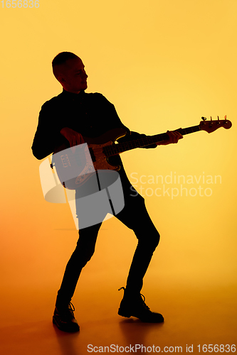 Image of Silhouette of young caucasian male guitarist isolated on orange gradient studio background in neon light