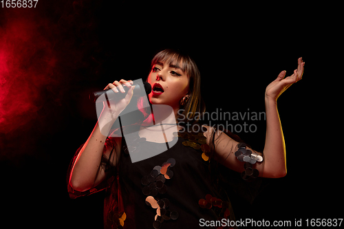 Image of Caucasian female singer portrait isolated on dark studio background in neon light