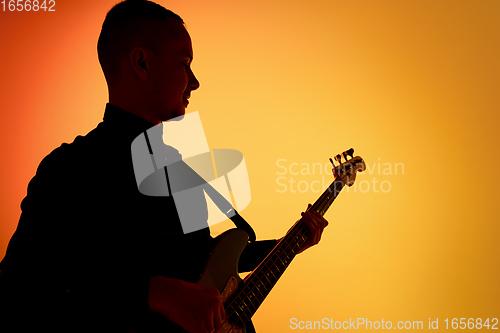 Image of Silhouette of young caucasian male guitarist isolated on orange gradient studio background in neon light