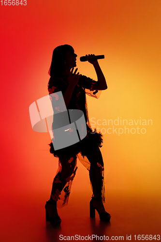 Image of Silhouette of young caucasian female singer isolated on orange gradient studio background in neon light