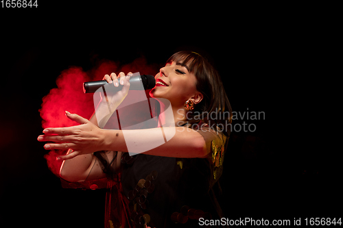 Image of Caucasian female singer portrait isolated on dark studio background in neon light