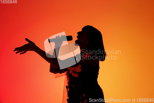 Image of Silhouette of young caucasian female singer isolated on orange gradient studio background in neon light