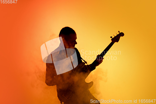 Image of Silhouette of young caucasian male guitarist isolated on orange gradient studio background in neon light