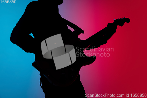 Image of Silhouette of young caucasian male guitarist isolated on blue-pink gradient studio background in neon light