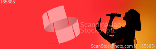 Image of Silhouette of young caucasian female singer isolated on orange gradient studio background in neon light