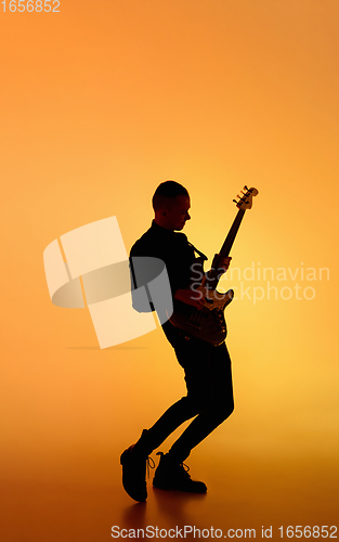 Image of Silhouette of young caucasian male guitarist isolated on orange gradient studio background in neon light