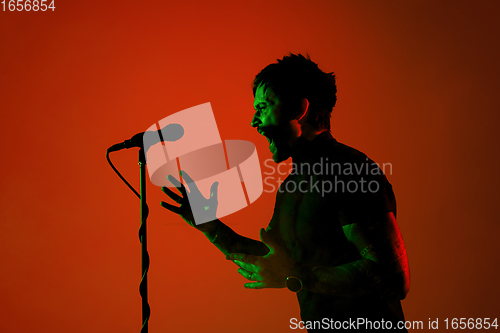 Image of Silhouette of young caucasian male singer isolated on orange gradient studio background in neon light