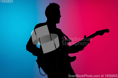 Image of Silhouette of young caucasian male guitarist isolated on blue-pink gradient studio background in neon light