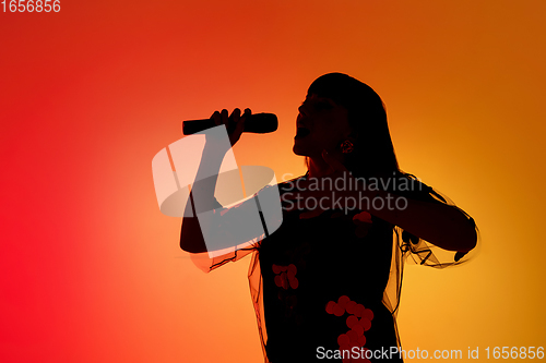 Image of Silhouette of young caucasian female singer isolated on orange gradient studio background in neon light