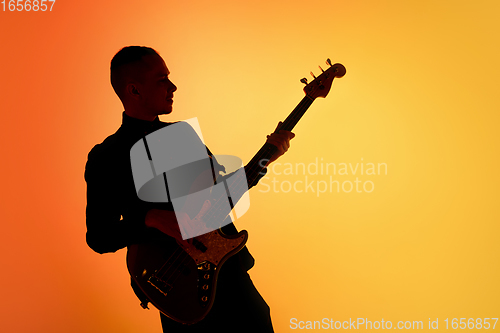 Image of Silhouette of young caucasian male guitarist isolated on orange gradient studio background in neon light