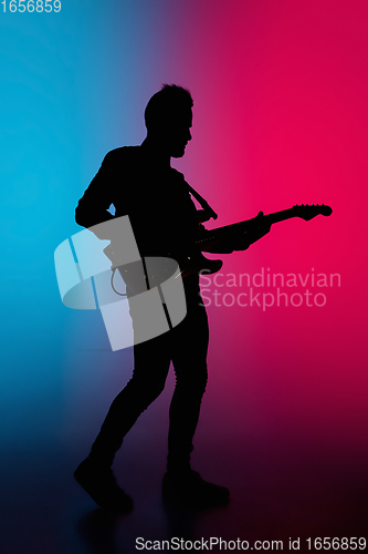 Image of Silhouette of young caucasian male guitarist isolated on blue-pink gradient studio background in neon light