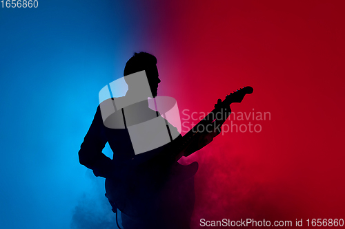 Image of Silhouette of young caucasian male guitarist isolated on blue-pink gradient studio background in neon light