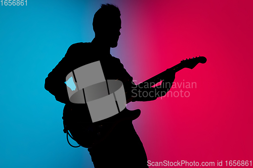 Image of Silhouette of young caucasian male guitarist isolated on blue-pink gradient studio background in neon light